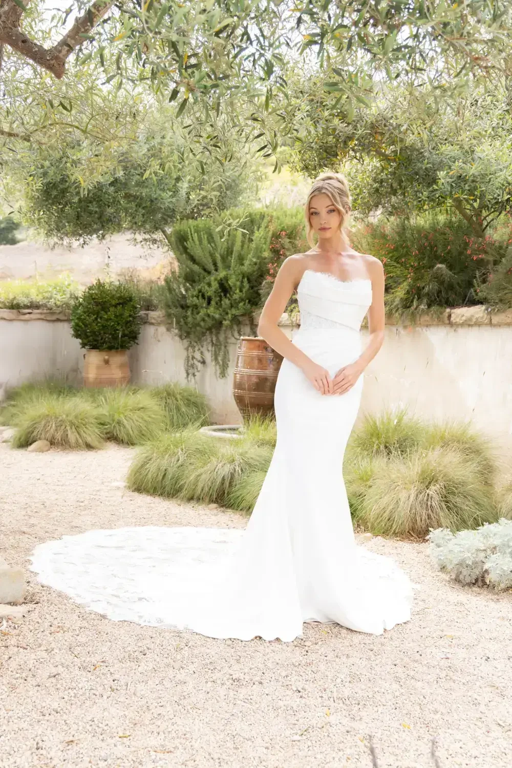 A woman in a white wedding dress poses outdoors in a garden setting.